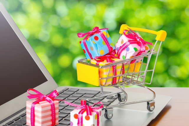 パソコンの前に小さなプレゼントが沢山入ったショッピングカートのイメージ図